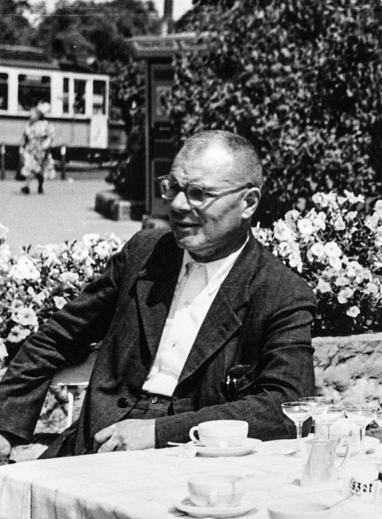 A man sitting at a table outside, with a cup of presumably coffee in front of him.